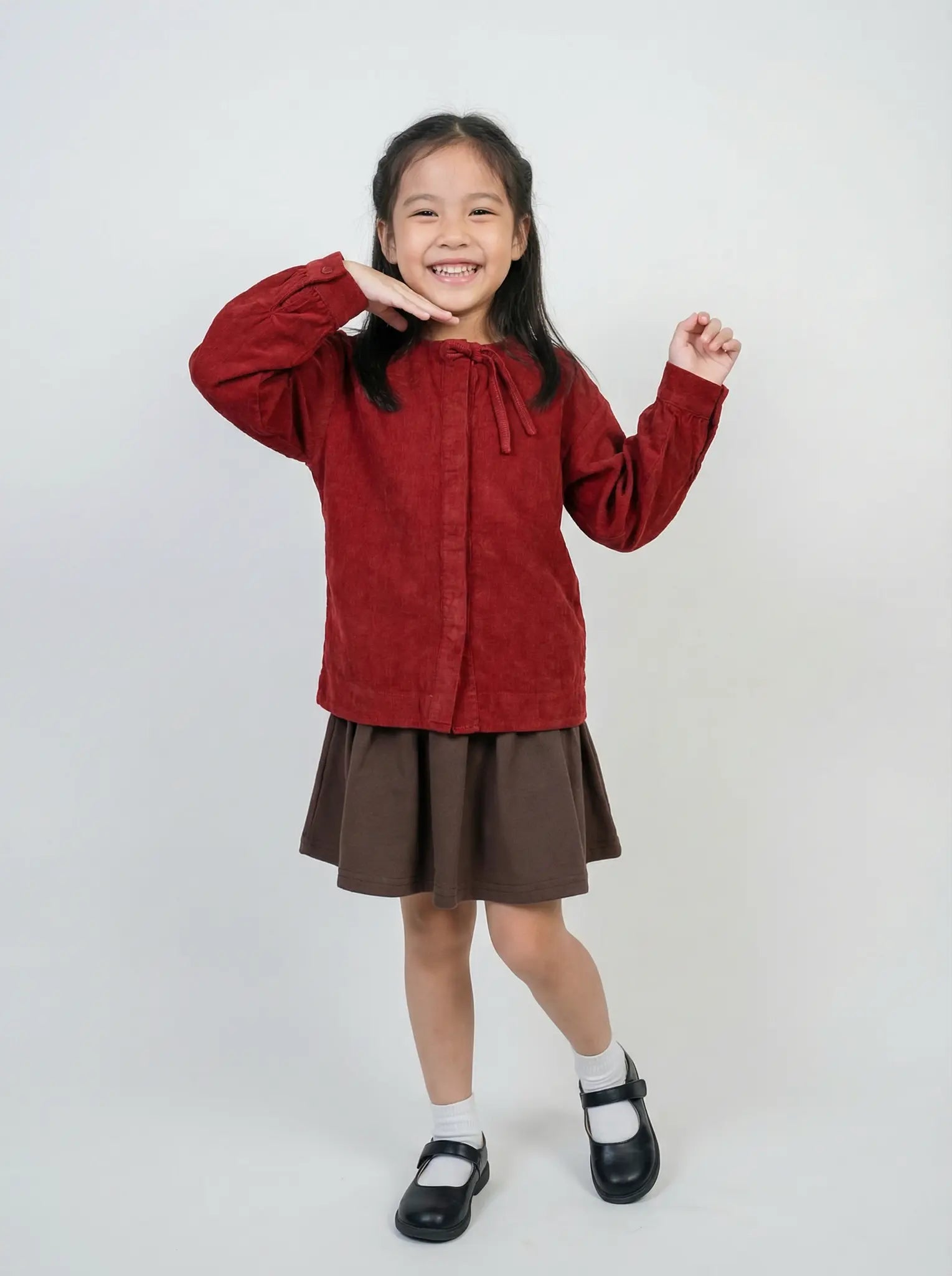 Young girl wearing a red sweater and brown skirt on a white background