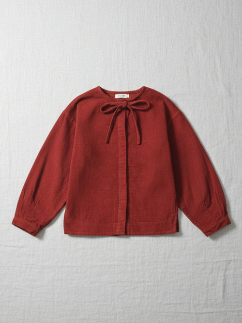 Children's long-sleeve top in a deep red corduroy fabric featuring a round neckline with a matching corduroy bow tie and hidden button placket