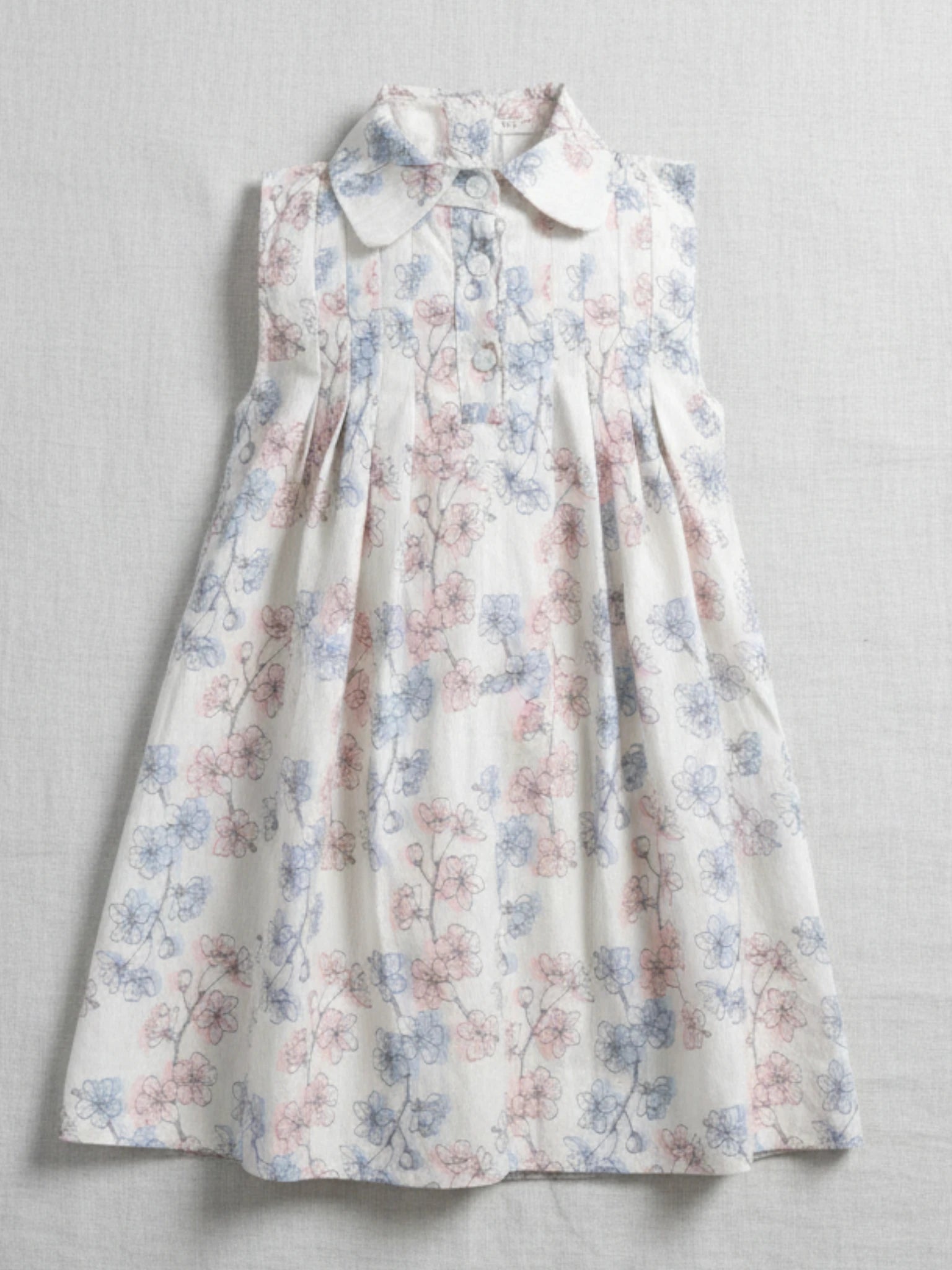 Kids sleeveless white A-line dress with a Peter Pan collar, front buttons, and a delicate pink and blue floral botanical print.