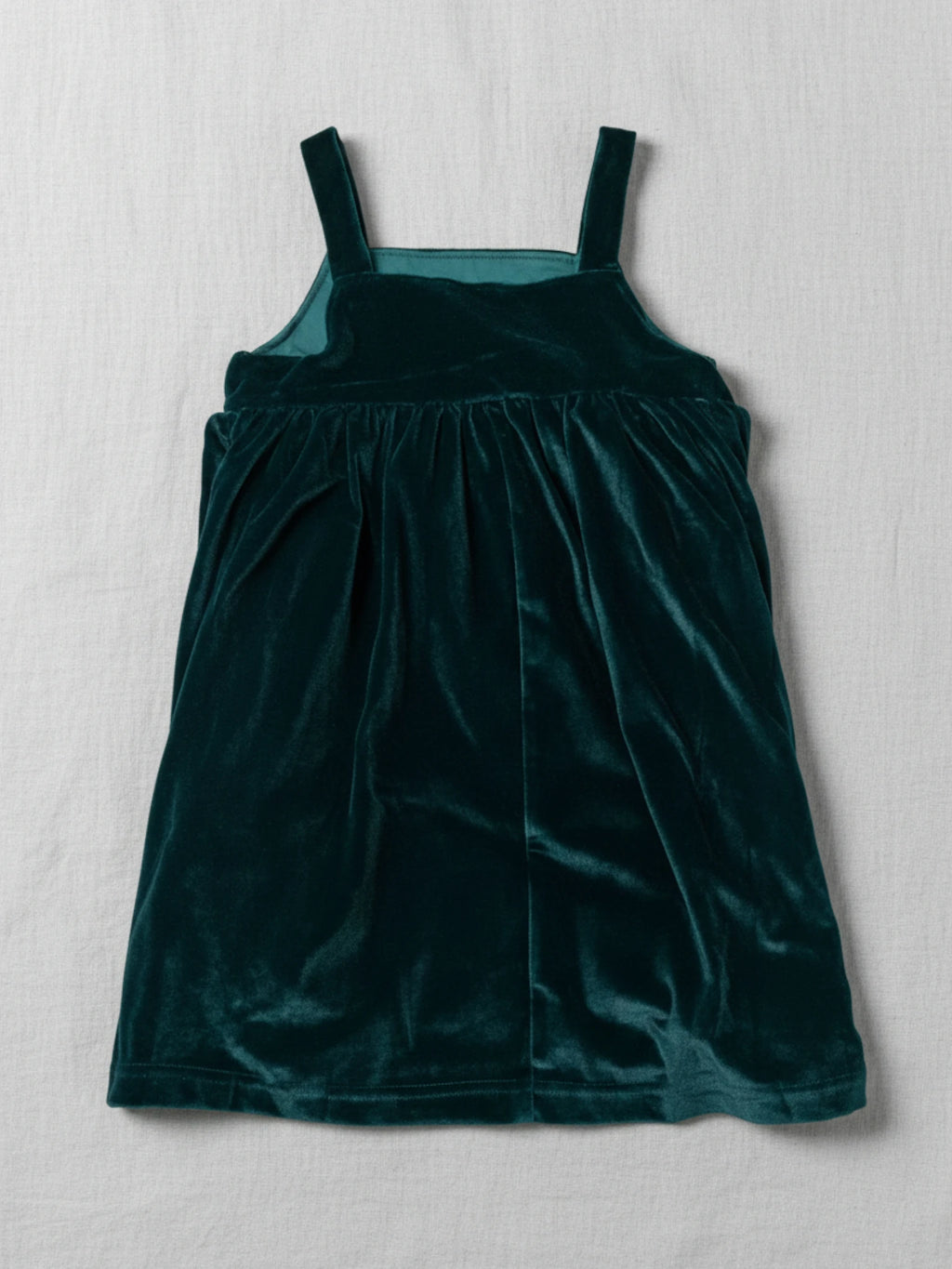 sleeveless emerald green velvet pinafore dress with a square neckline on a white studio background.