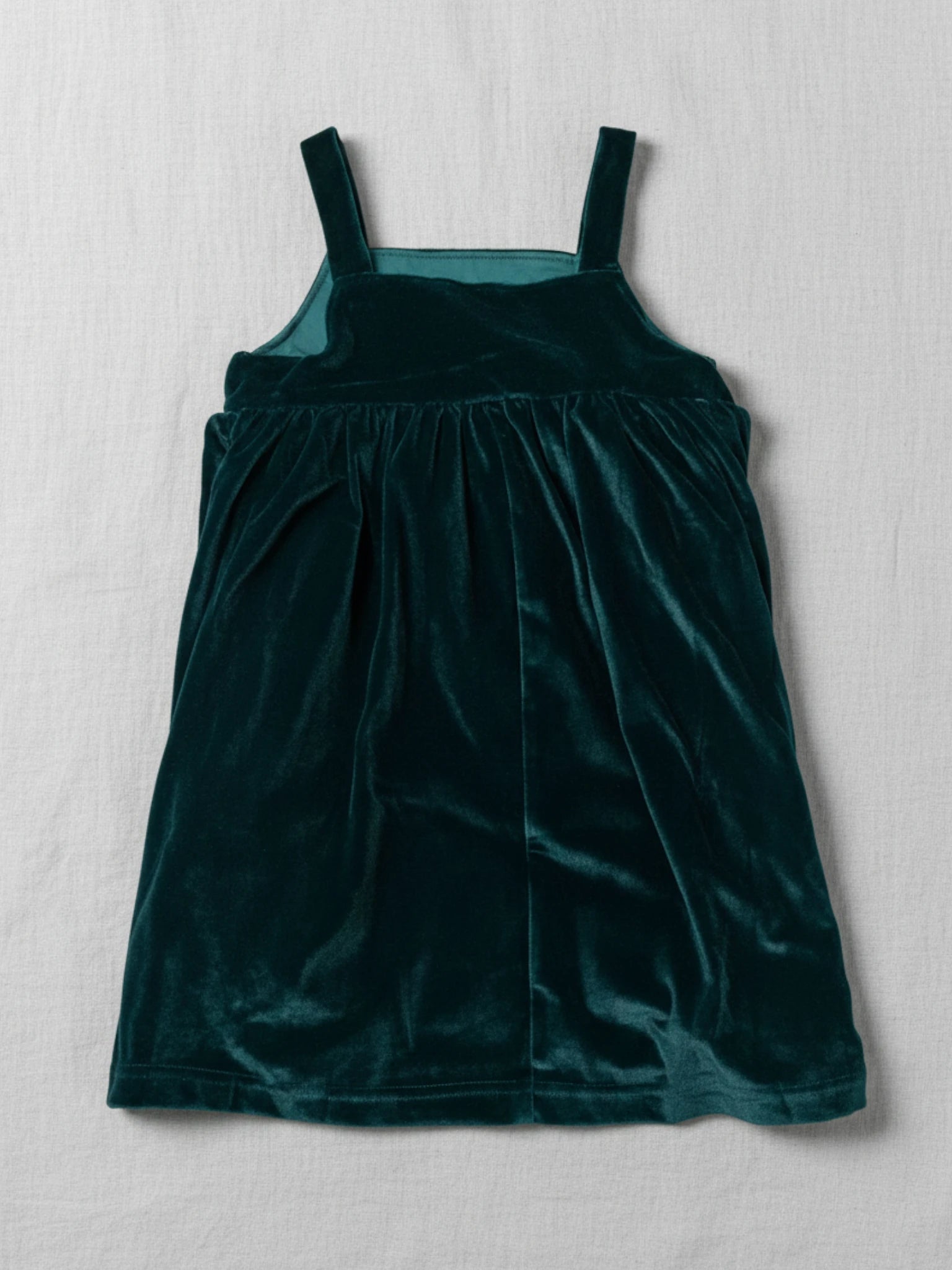 sleeveless emerald green velvet pinafore dress with a square neckline on a white studio background.