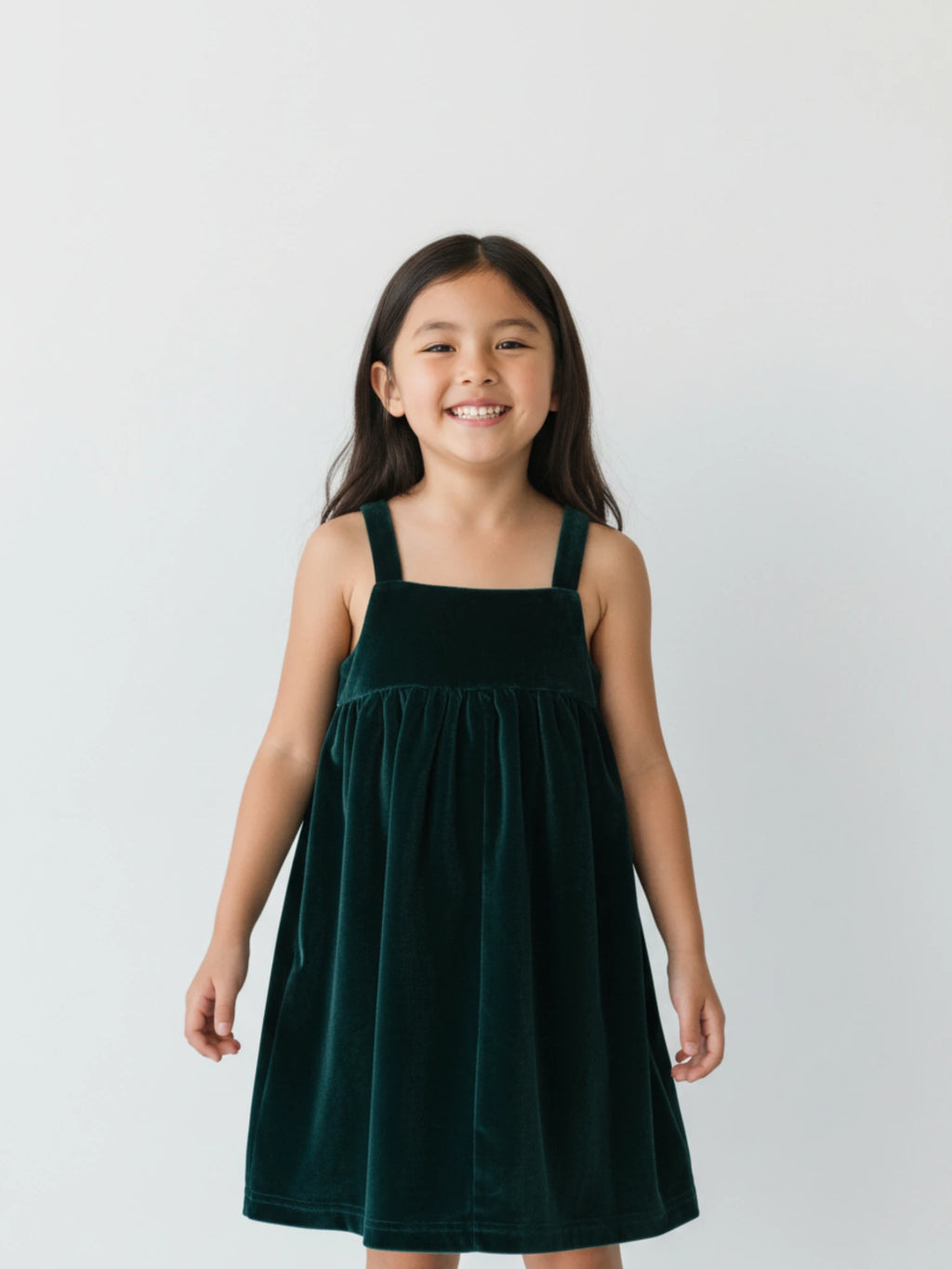 sleeveless emerald green velvet pinafore dress with a square neckline on a white studio background.