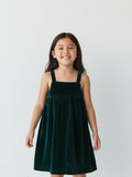 sleeveless emerald green velvet pinafore dress with a square neckline on a white studio background.