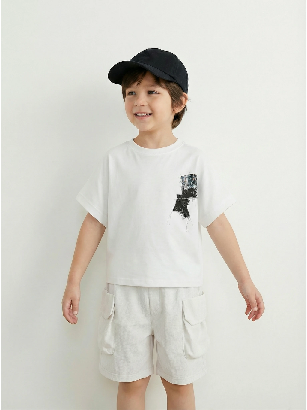 Kids white short-sleeve cargo shorts with an elasticated waistband and large side flap pockets displayed on a neutral textured background.