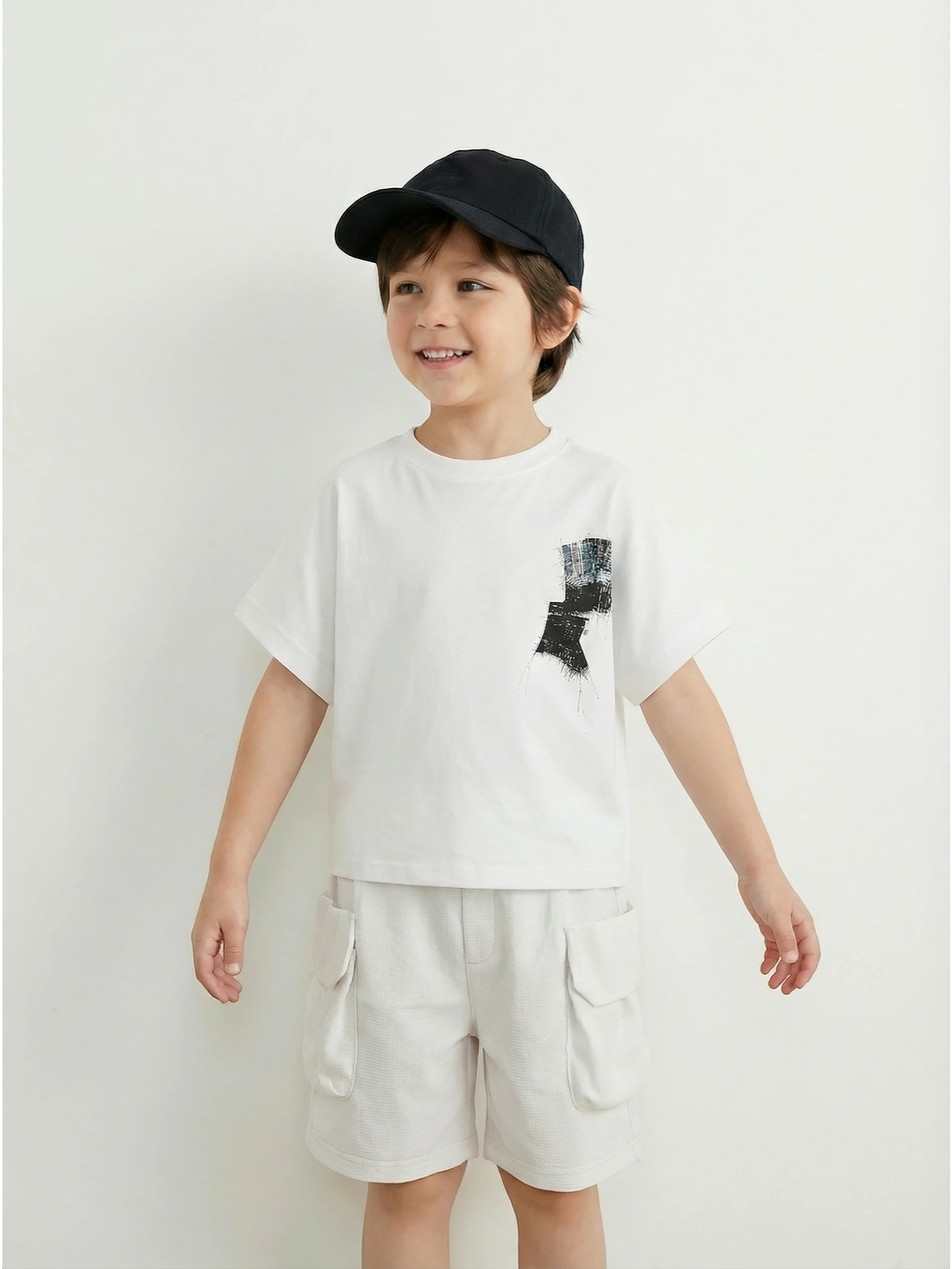 Kids white short-sleeve cargo shorts with an elasticated waistband and large side flap pockets displayed on a neutral textured background.